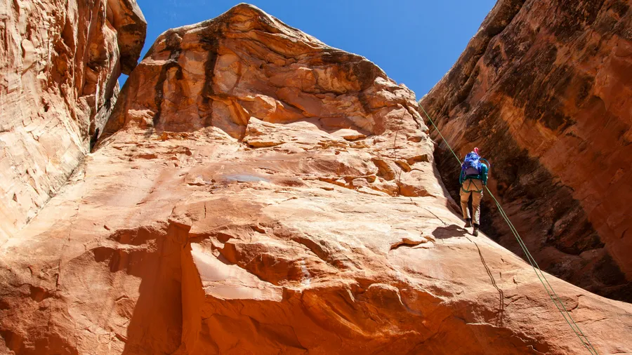 Persona descendiendo por un cañón de roca roja en Utah.
