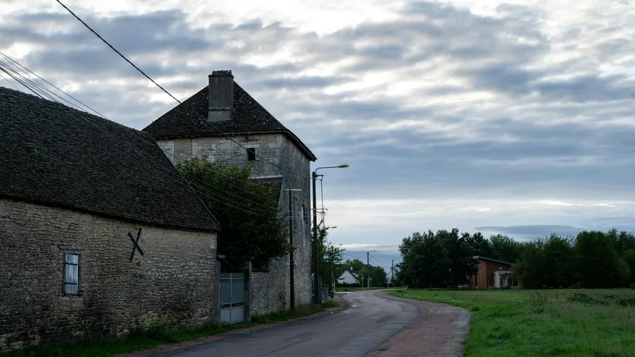 Un camino rural que pasa junto a edificios de piedra bajo un cielo nublado.