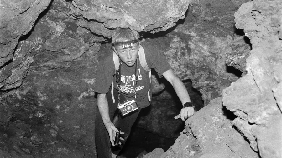 Persona explorando una cueva oscura y rocosa con una linterna en la cabeza.